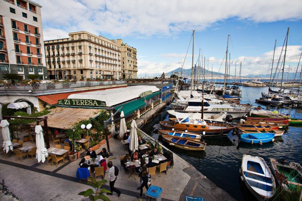 Ristorante Zi Teresa a Borgo Marinari, Napoli: terrazza sul porticciolo con tavoli all’aperto, barche colorate e Vesuvio sullo sfondo.